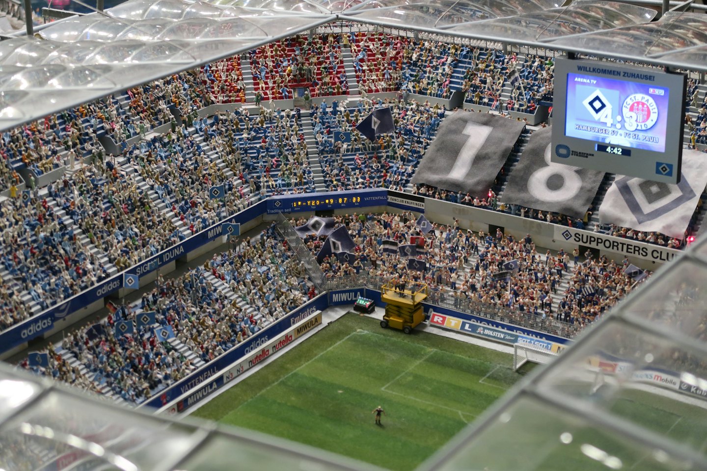 A detailed miniature football stadium model with packed fan stands.